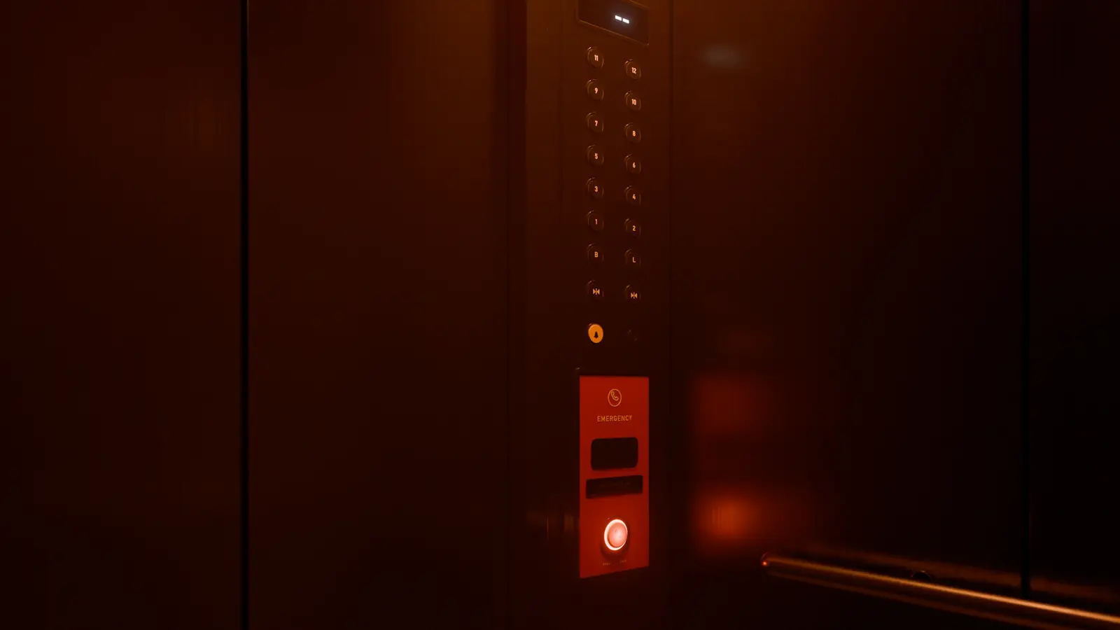An elevator car with the lights out, lit only by the red glow of its emergency panel.